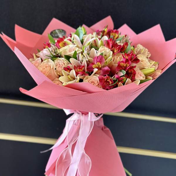 Pink-wrapped bouquet of peach roses and mixed lilies