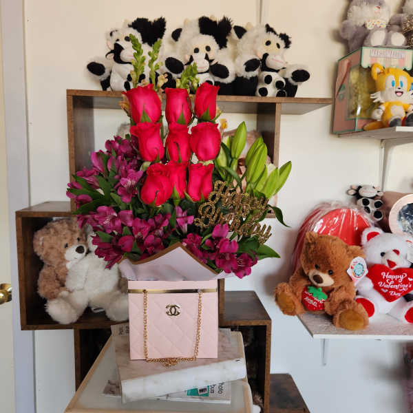 Pink roses and purple flowers arranged in a gift box with a gold Happy Birthday topper.