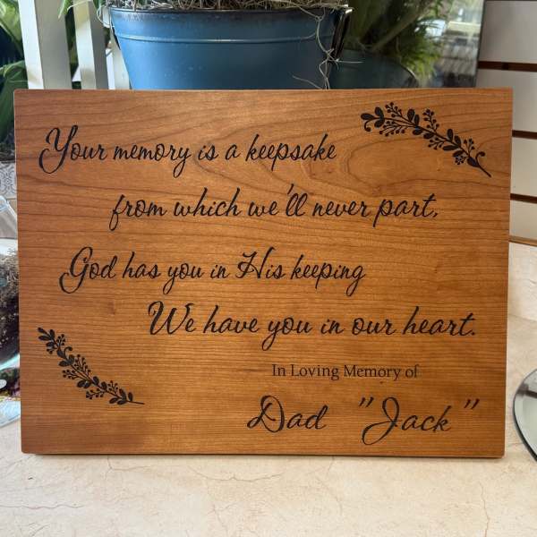 Wood memorial plaque with engraved sympathy message and potted plants nearby