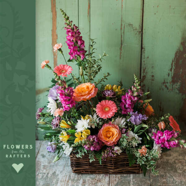 Mixed flower arrangement in a wicker basket with pink, orange, yellow, and white blooms