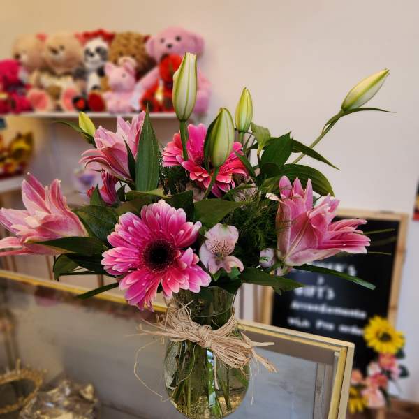 Pink gerbera daisies and lilies in a glass vase with raffia tie