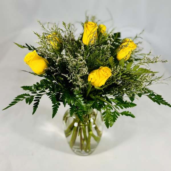 Yellow roses in a clear glass vase with airy greenery
