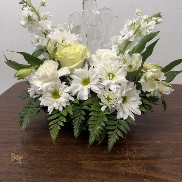 White floral arrangement with daisies and roses around a clear angel figurine