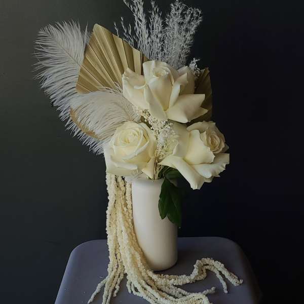 Cream roses in a white vase with dried feathers and fan leaves