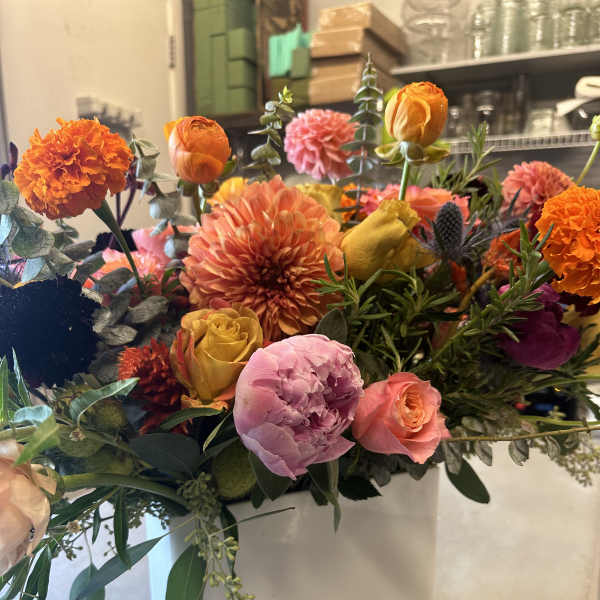 Mixed bouquet of orange, pink, and yellow flowers in a white box