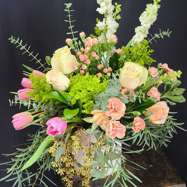 Mixed bouquet with roses, tulips, and tall white spikes in a white container