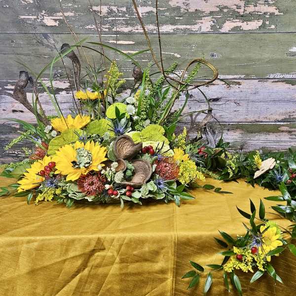 Yellow floral arrangement with greenery and decorative pods on a table