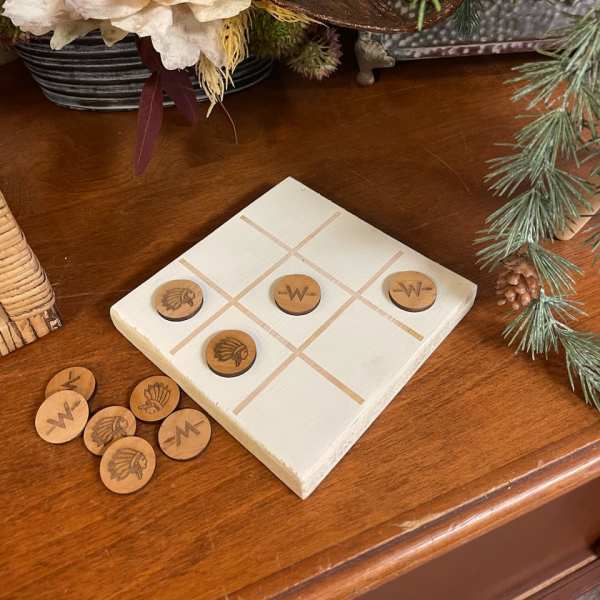 Tic-tac-toe board with wooden game pieces on a table beside a floral arrangement