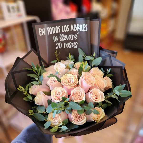 Bouquet of pale pink roses wrapped in black paper with greenery