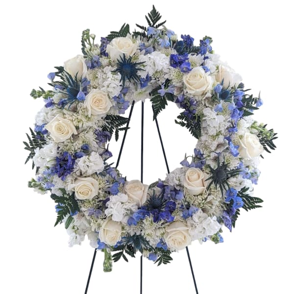 Circular floral wreath with white roses and blue flowers on a stand