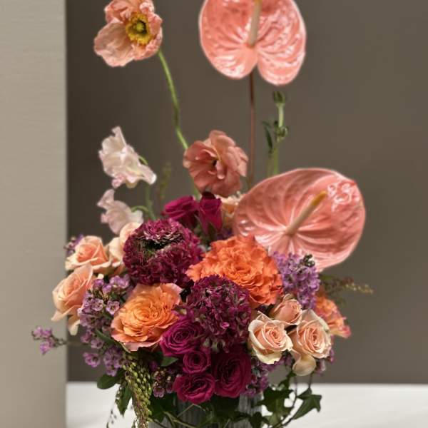 Pink and orange floral arrangement in a gray vase with tall anthuriums