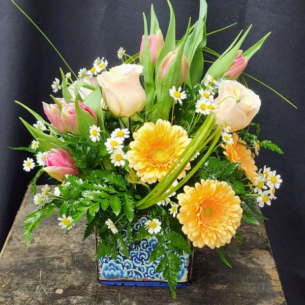 Mixed bouquet with pink tulips, pale roses, and yellow daisies in a patterned vase