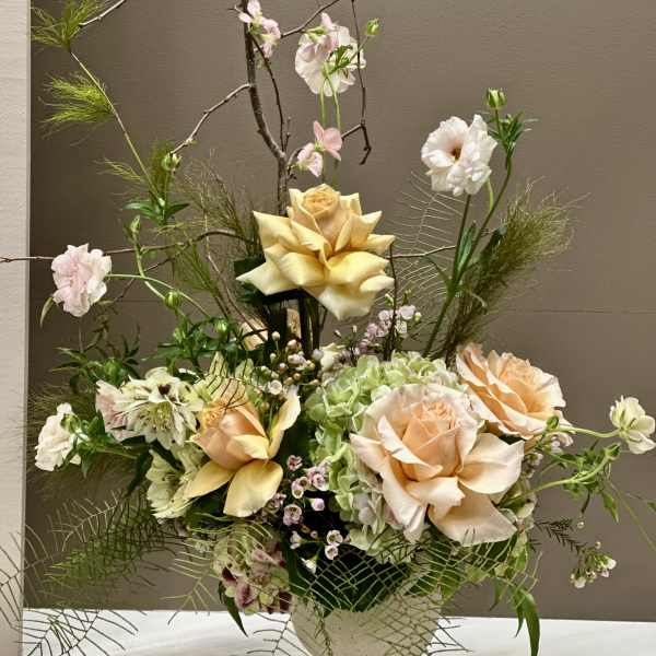 Tall floral arrangement with peach roses, pale blooms, and branching stems in a vase