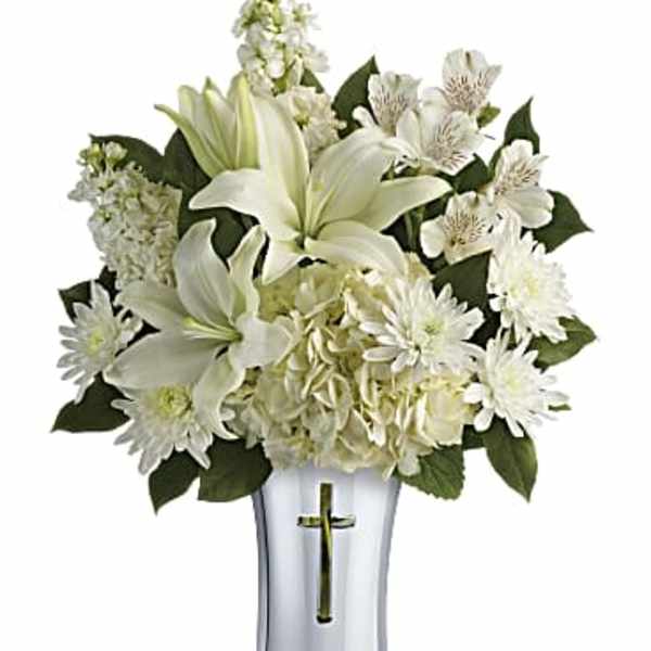 White floral arrangement in a silver vase with a cross emblem