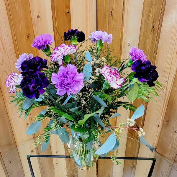Tall clear vase of purple and lavender carnations with white-edged blooms and mixed foliage