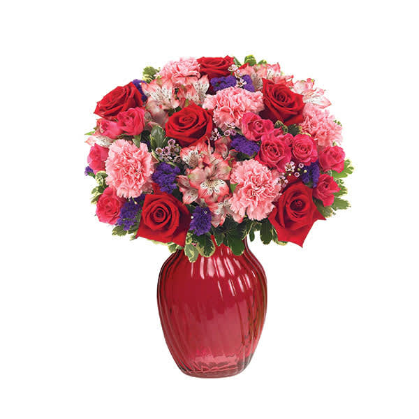 Bouquet of red roses, pink carnations, and purple filler in a red vase