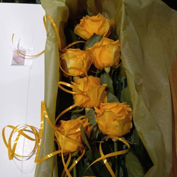 Bouquet of yellow roses wrapped in green paper with gold ribbon