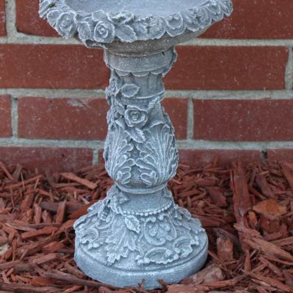 Decorative gray stone pedestal birdbath with floral reliefs