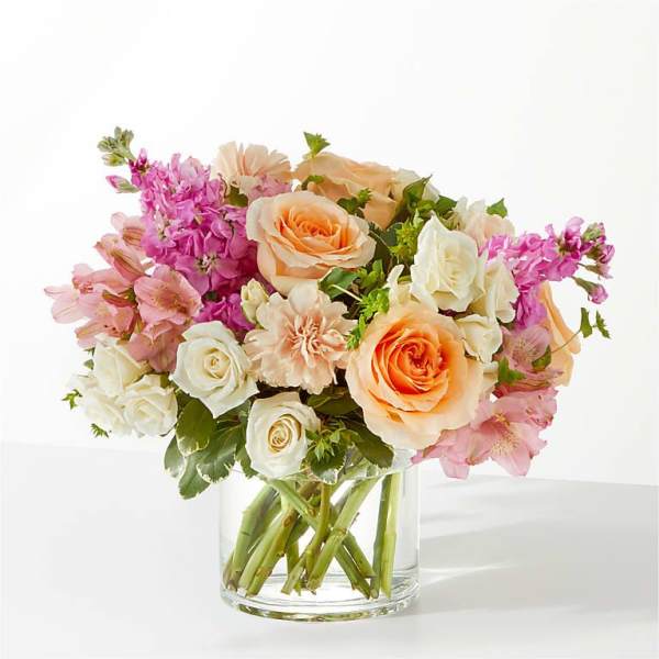 Bouquet of peach and white roses with pink flowers in a clear glass vase