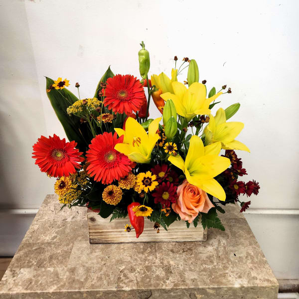 Mixed bouquet of red gerbera daisies and yellow lilies in a wooden box