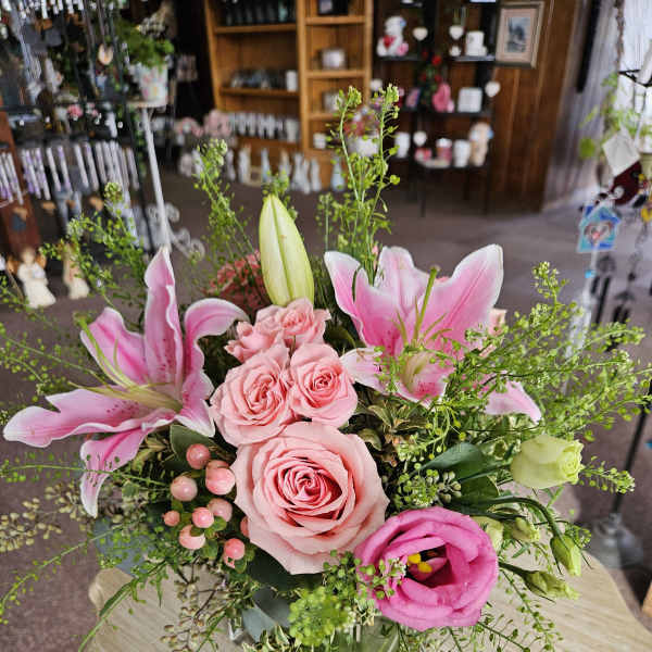 Pink lilies, roses, and lisianthus arranged in a clear glass cube vase