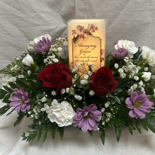 Floral arrangement with red roses, white and purple flowers, and a lit memorial candle