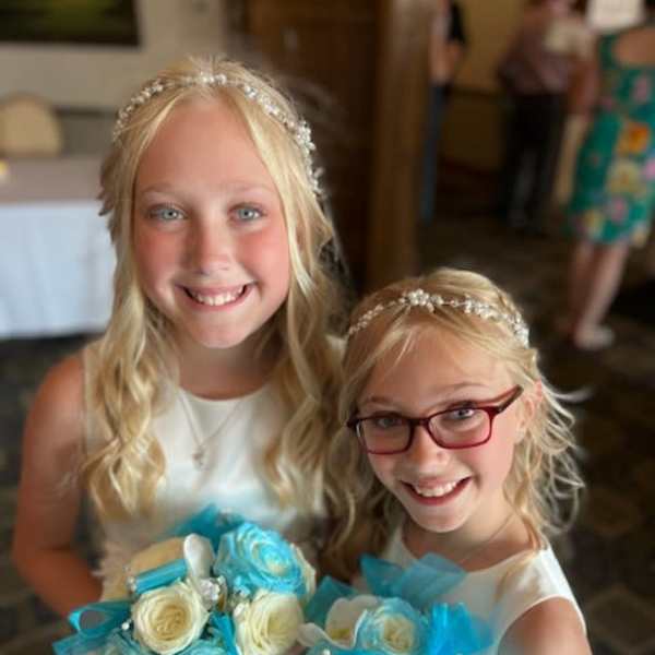 Two girls in white dresses holding small blue and white rose bouquets