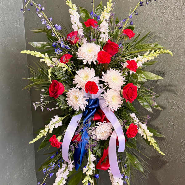 Tall standing spray of red roses, white mums, and blue accents with patriotic ribbons on an easel.