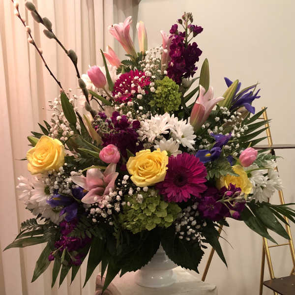 Large mixed flower arrangement in a white vase with pink, yellow, purple, and white blooms.