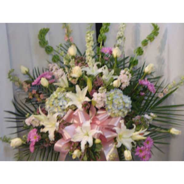 Large floral spray with white lilies, pink flowers, and a pink ribbon bow