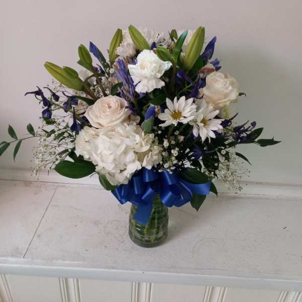 White and blue mixed bouquet in a glass vase with a blue ribbon
