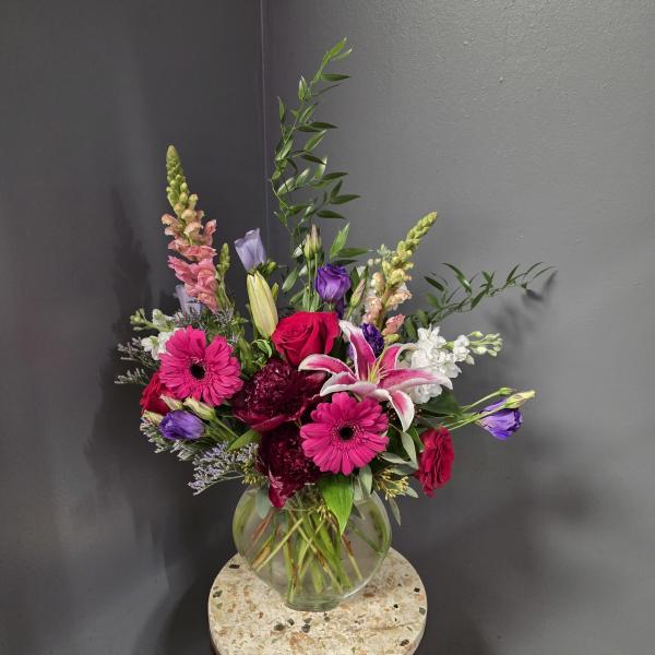 Mixed bouquet of pink, purple, white, and red flowers in a glass vase.