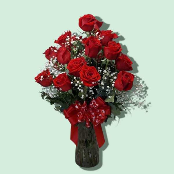 Red roses arranged in a glass vase with a red ribbon bow