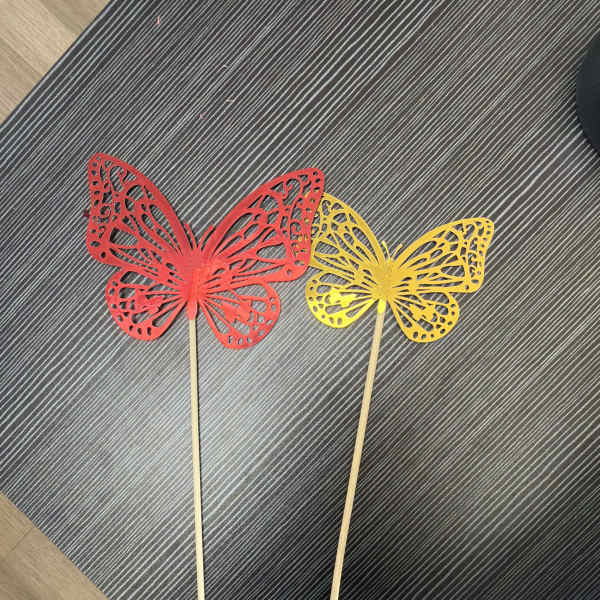 Two butterfly-shaped decorative picks on sticks, one red and one yellow