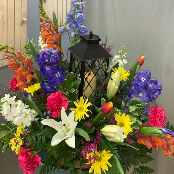 Colorful floral arrangement with lilies, daisies, and snapdragons around a black lantern