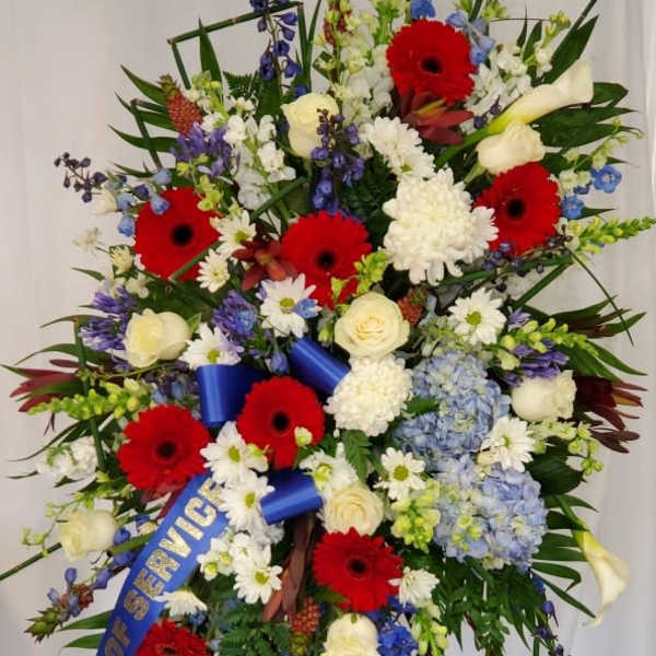 Large standing floral spray with red gerberas, white roses, and blue flowers
