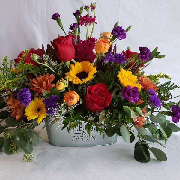 Mixed bouquet in a metal container with roses, sunflowers, and purple blooms