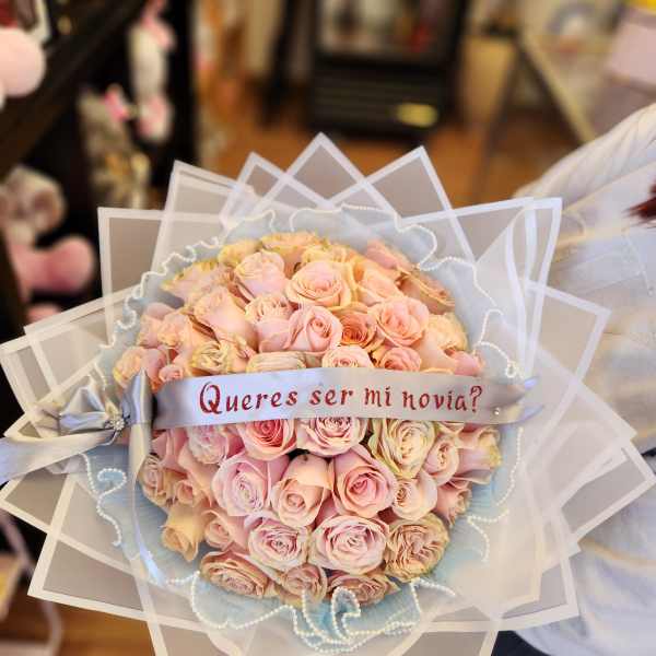 Bouquet of pale pink roses with a ribbon reading "Quieres ser mi novia?"