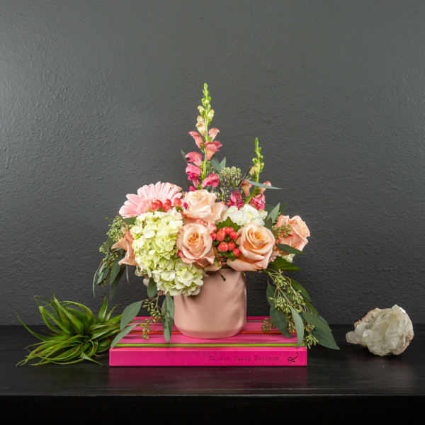 Peach roses and pink flowers in a blush vase on a pink book