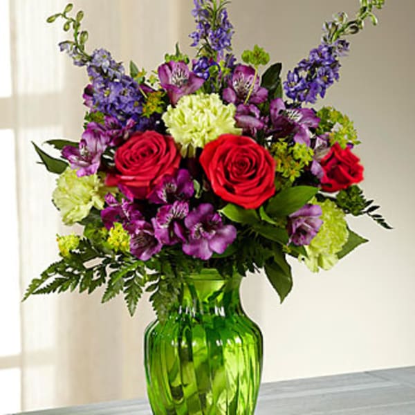 Bouquet of red roses, purple flowers, and green carnations in a green glass vase