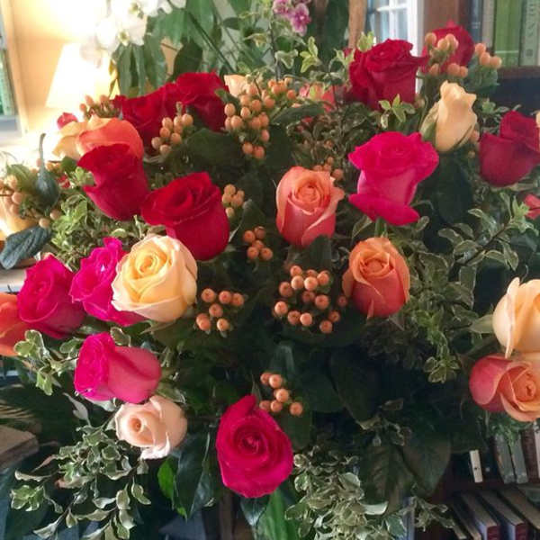 Large bouquet of red, pink, and peach roses with berries in a clear glass pedestal vase