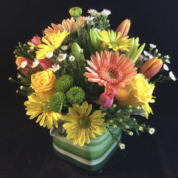 Mixed bouquet of yellow, orange, pink, and white flowers in a green striped vase