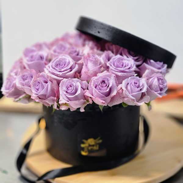 Lavender roses arranged in a black round hat box