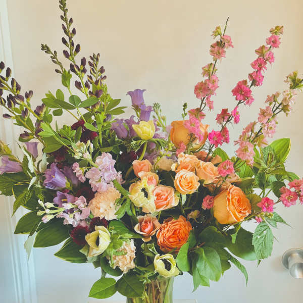 Mixed bouquet of orange, pink, and purple flowers in a clear glass vase