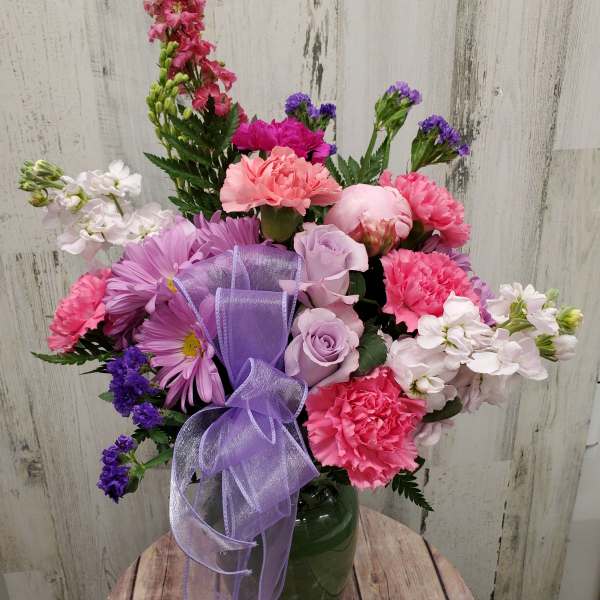Mixed pink and purple bouquet in a green vase with a lavender ribbon