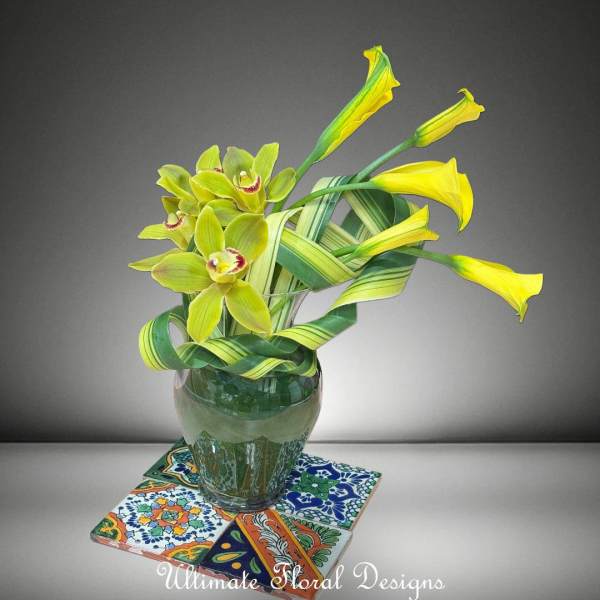 Yellow-green orchids in a glass vase on patterned tiles