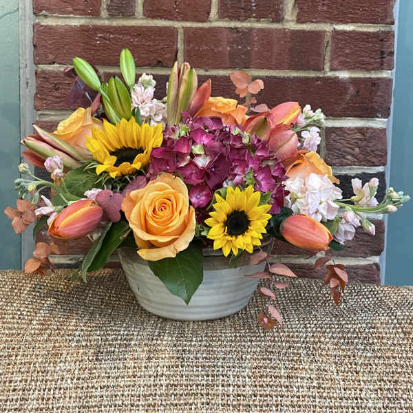 Mixed bouquet in a white bowl vase with sunflowers, roses, hydrangea, and tulips