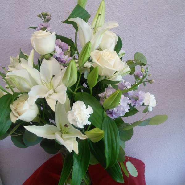 White lilies and roses arranged in a glass vase with lavender accents.