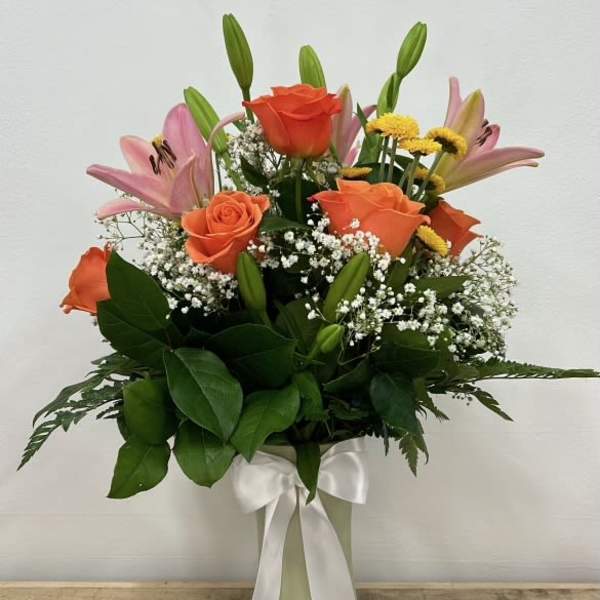 Orange roses and pink lilies in a white vase with a ribbon