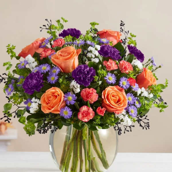 Mixed bouquet of orange roses, purple carnations, and small lavender daisies in a glass vase